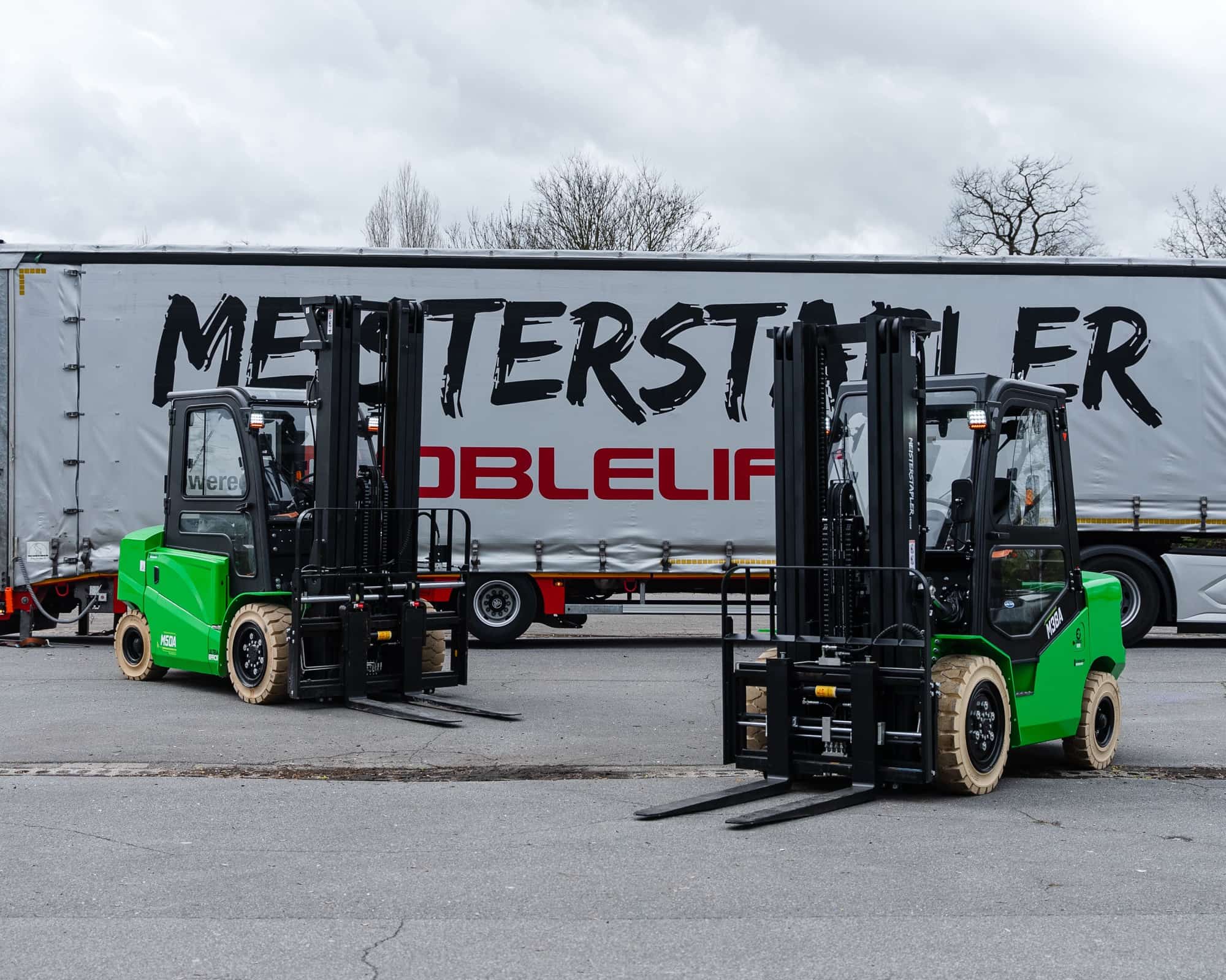 Zwei grüne Meisterstapler vor einem Lkw mit Meisterstapler-Plane